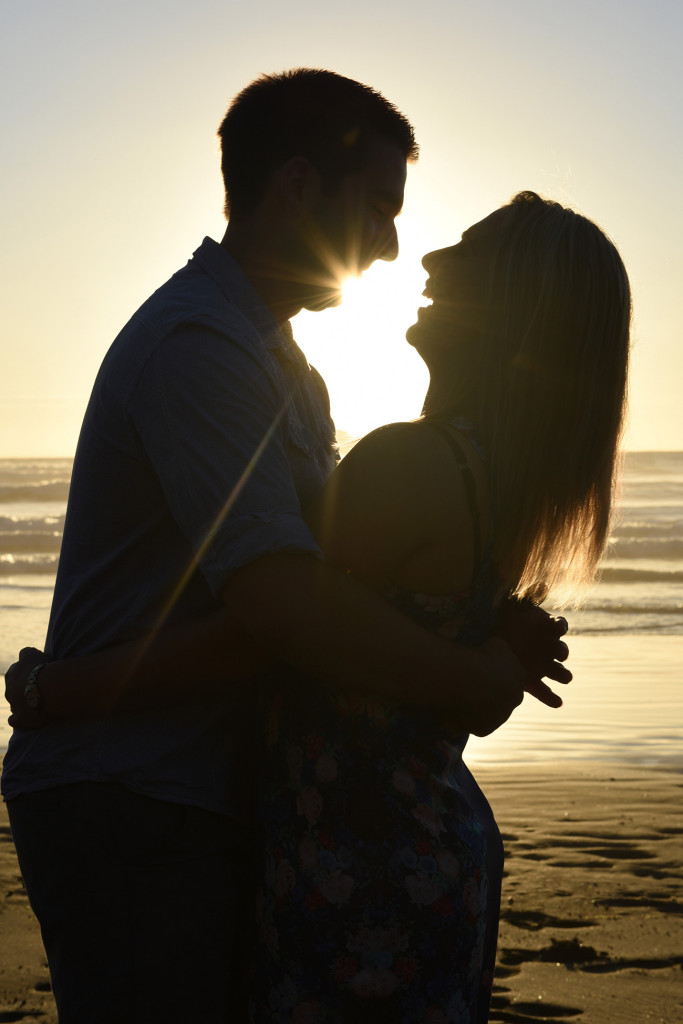 couple laughing silhouette with sun and sea behind