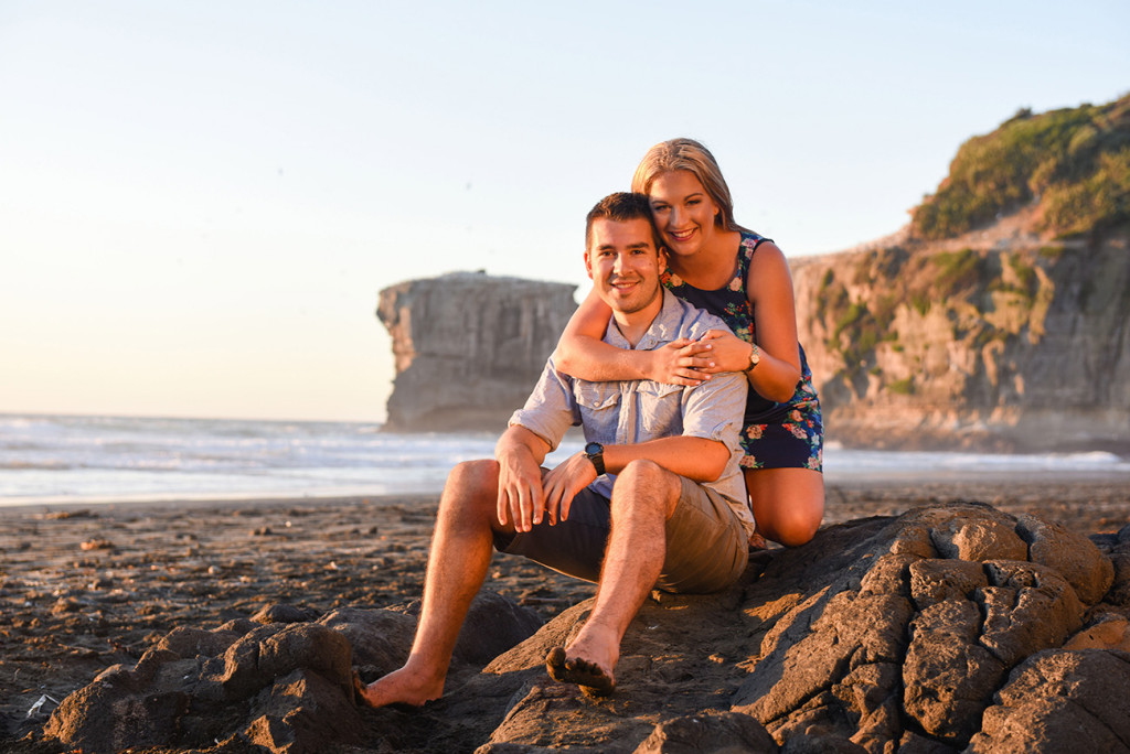 couple hugging by Muriwai beach while sunset and its orange light