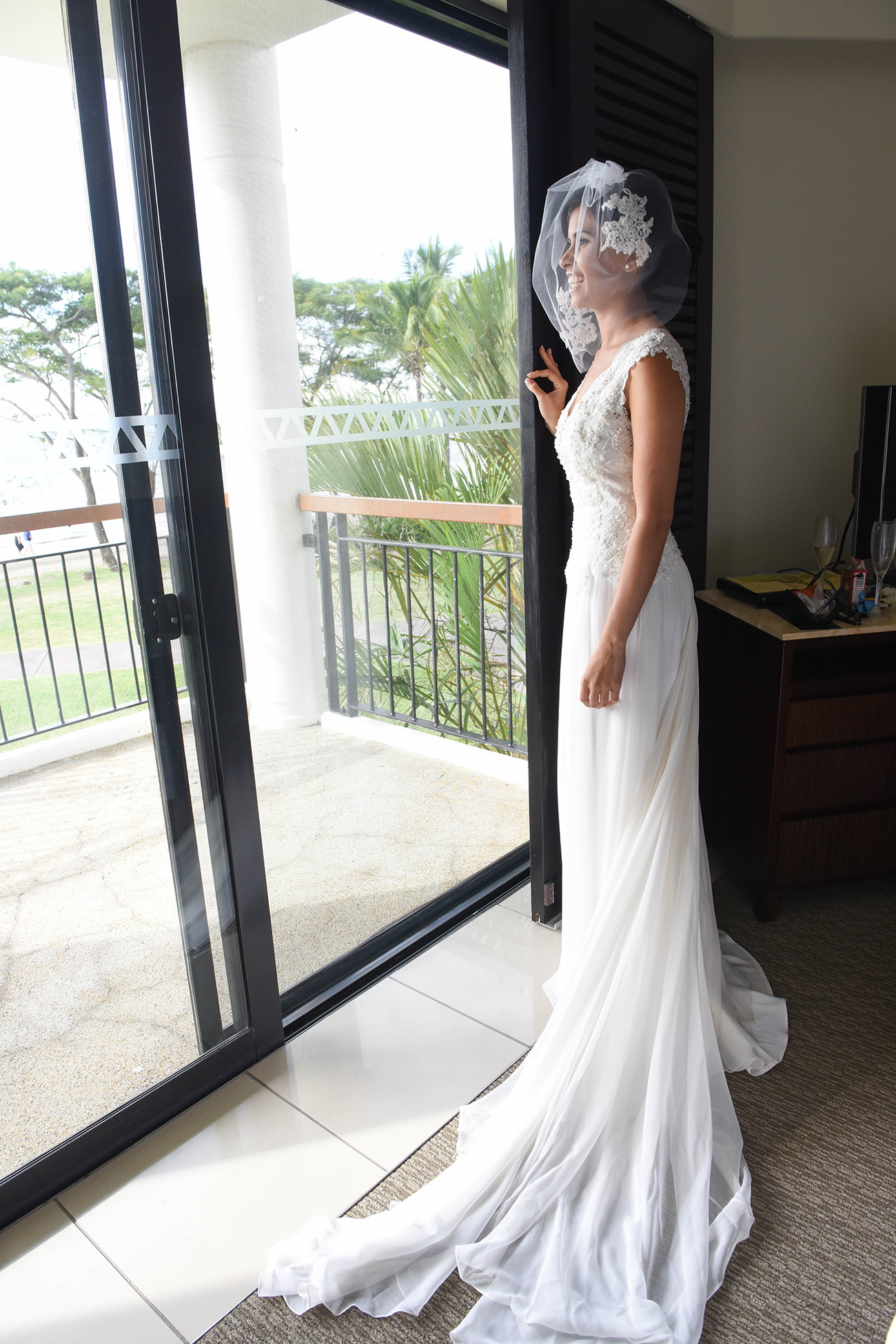 In front of the window Bride smiling in her beautiful wedding dress and her veil