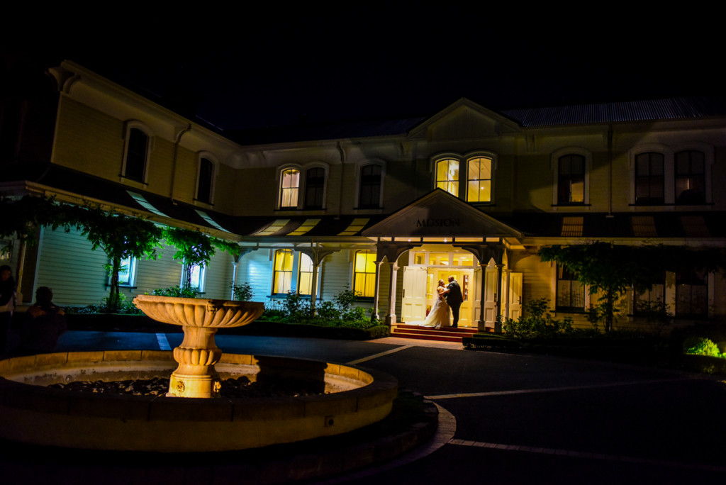 The bride and groom under the warm glow of the Mission Estate Winery house