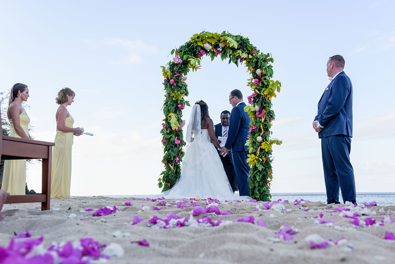 The bride and the groom are getting married on the beach At Paradise Cove Island resort in the Yasawas, Fiji with a beautiful arch made of tropical flowers