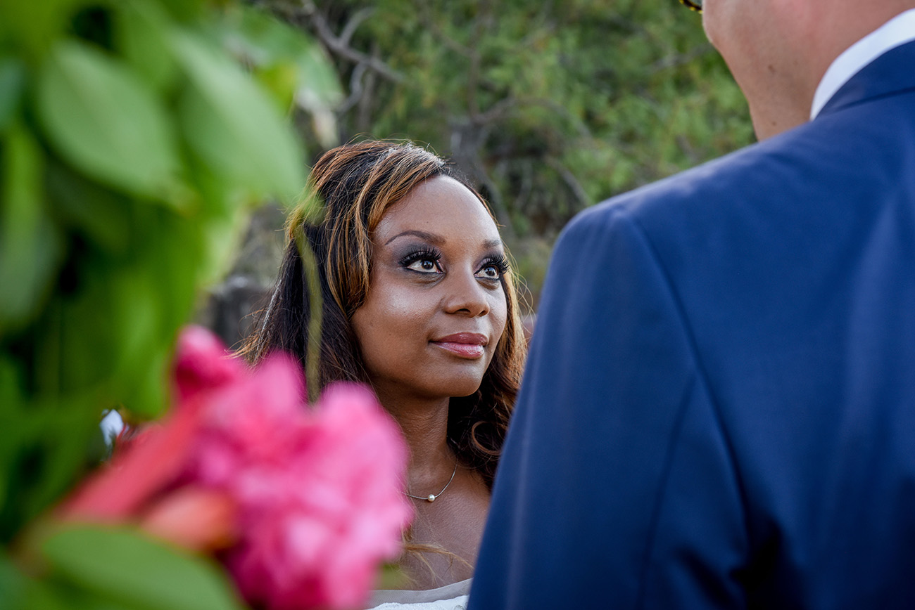 PORTRAIT OF THE bride smiling while looking at the groom with pink flower in the foreground At Paradise Cove Island resort in the Yasawas, Fiji