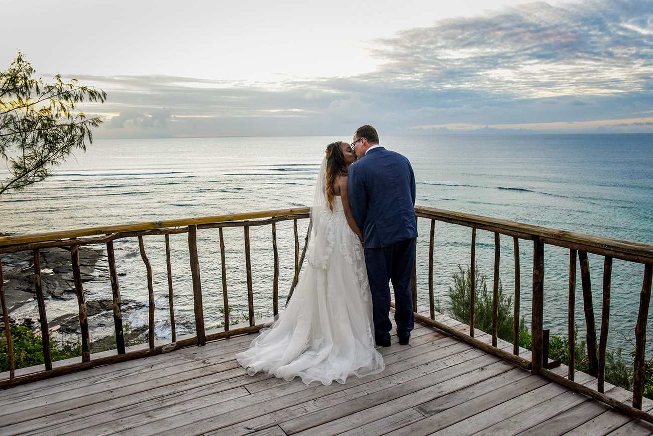 The bride and the groom are kissing at sunset point on the top of the island withe the ocean in front of them at Paradise Cove island resort in the Yasawas in Fiji photographed by Anais Photography