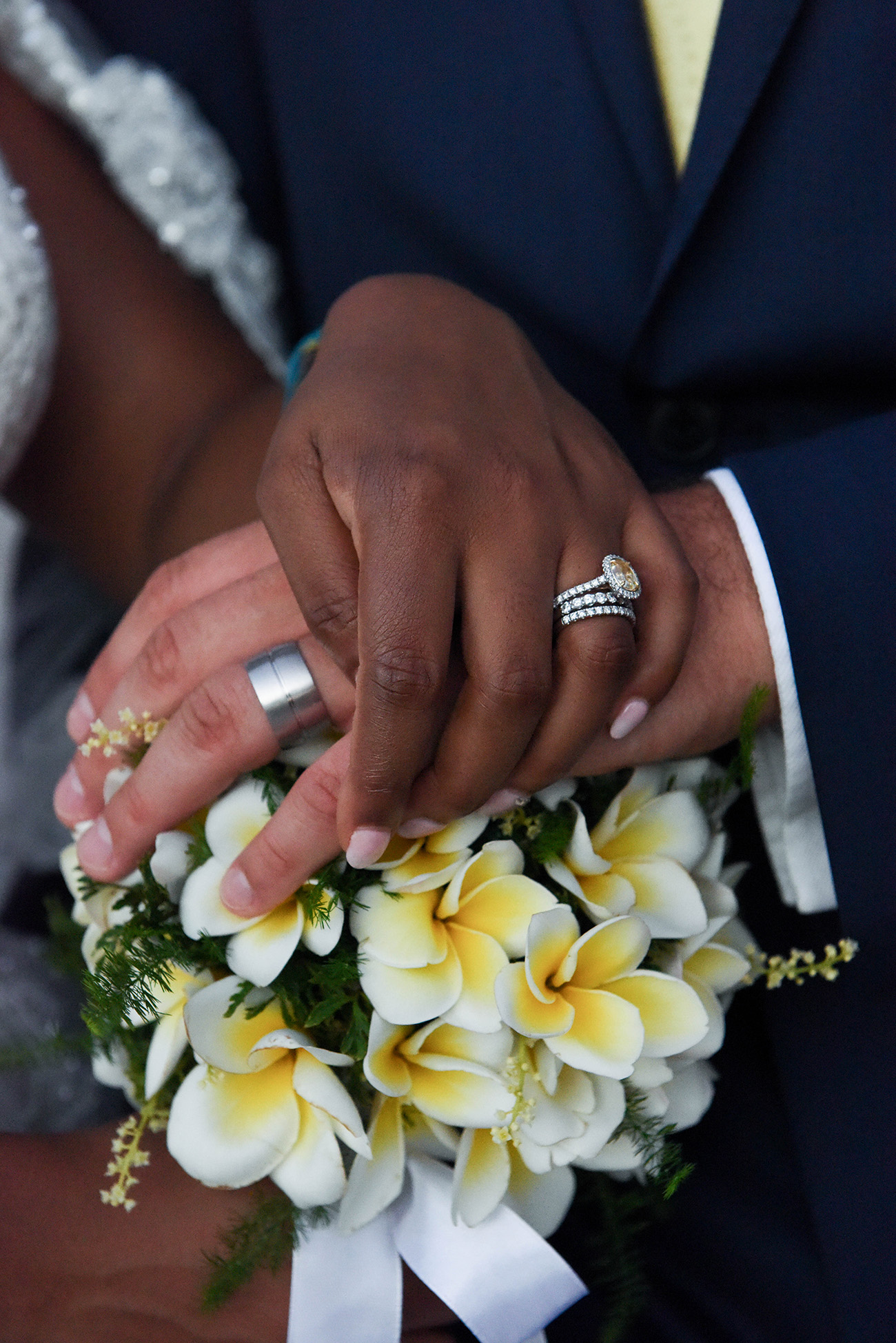 The bride and groom's hand with their wedding rings over the bride's bouquet made of frangipani flowers