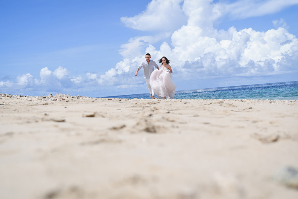 Bride and groom are running along the beach and its white sand at Paradise Cove island resort, Fiji
