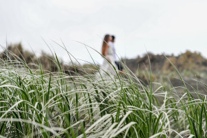 Bride and groom stroll in grass at Karekare Beach Auckland NZ