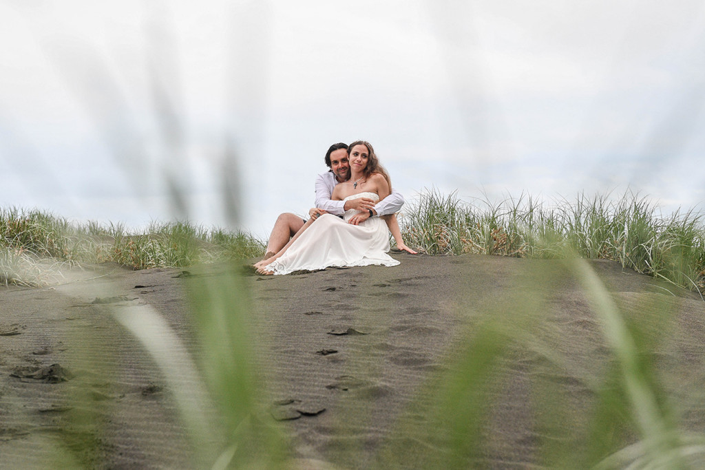 Bride and groom sit on the black sand beaches of Karekare NZ Auckland