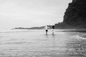 Black and white photo of newly eloped couple walking into the sea Karekare Beach Auckland NZ