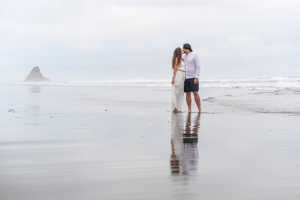 Newly eloped couple kiss on black sand Karekare Beach