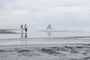 Newly eloped couple walk hand-in-hand in KArekare black sand Auckland