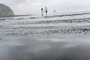 Newly eloped couple walk hand-in-hand in KArekare black sand Auckland
