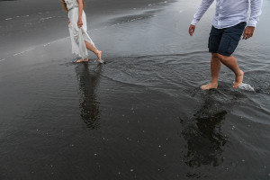 Married couple walk together in black sand beach Karekare NZ Auckland