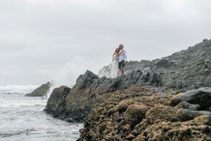 Newly married couple hug standing on rocks at Karekare NZ Auckland