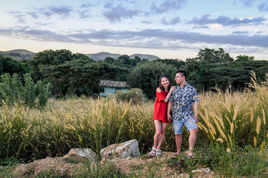 Loving Asian couple stand against deserted cabin in engagement photoshoot in Fiji countryside