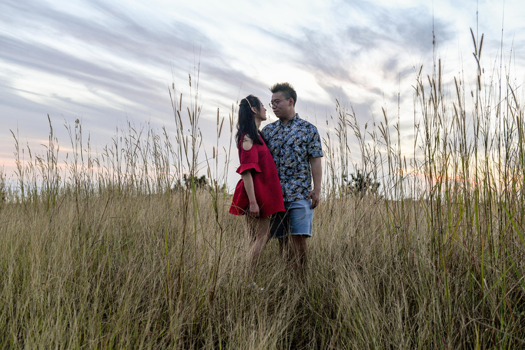 Young asian couple stare at each other in engagement photoshoot in countryside Fiji agains a fiery sunset