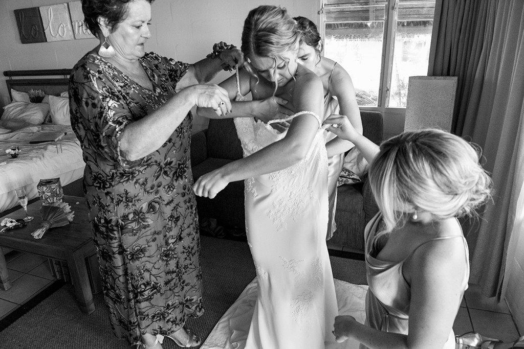 Black and white photo of Mom and bridesmaids helping bride wear wedding gown