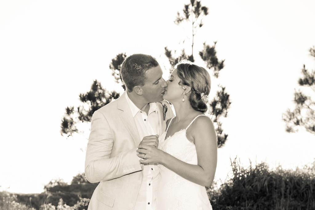 Sepia tone photo of bride and groom kissing against the sun