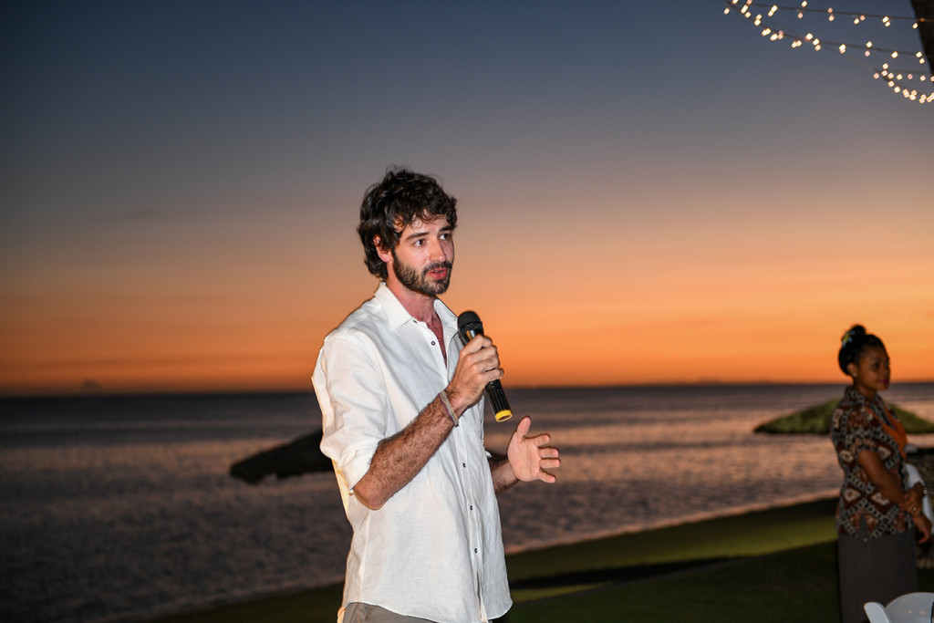 Groom's brother gives speech against orange sunset at beach wedding