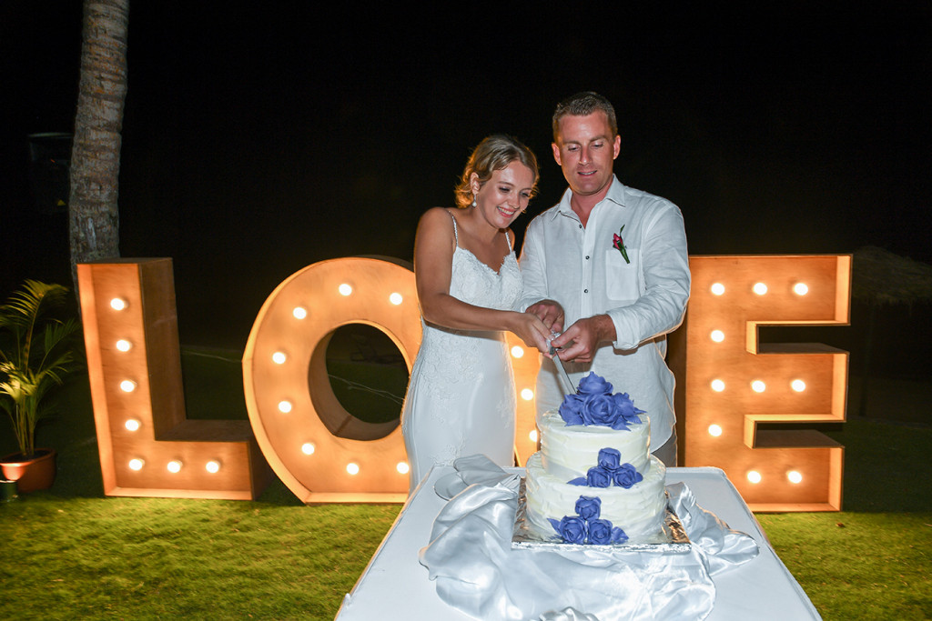 Bride and groom cut cake in front of Love poster and sea