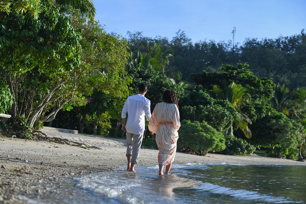 Newly wed couple wade in the ocean against Fiji greenery at Likuliku Honeymoon Resort