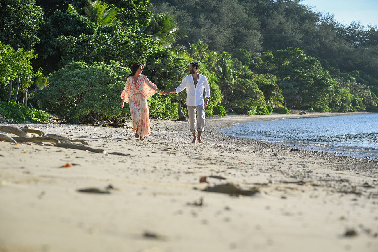 Newly wed couple hold hands and stroll on the beach