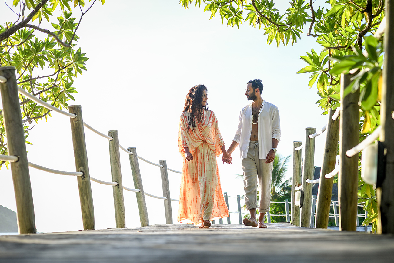 Newly married couple hold hands and stroll on wooden bridge in Likuliku Resort