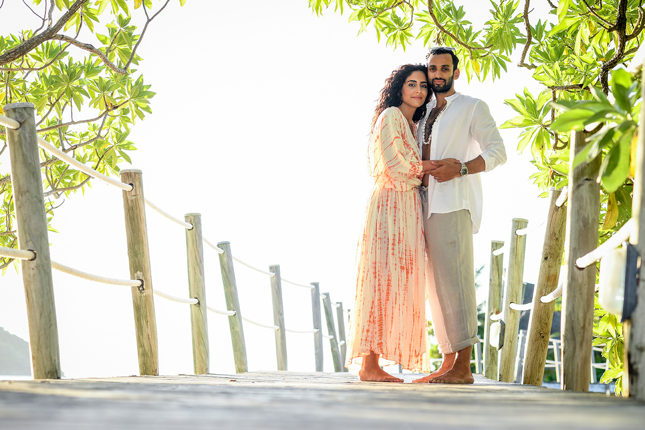 Newly married couple stand on wooden bridge covered in green at Likuliku Honeymoon resort