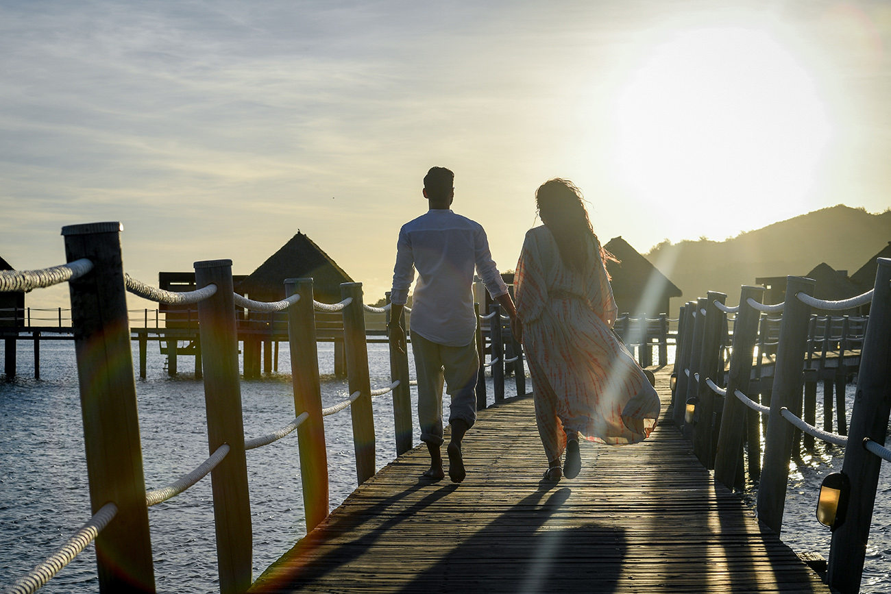 Newly married couple walk towards the sunset on wooden bridge in Fiji Likuliku resort