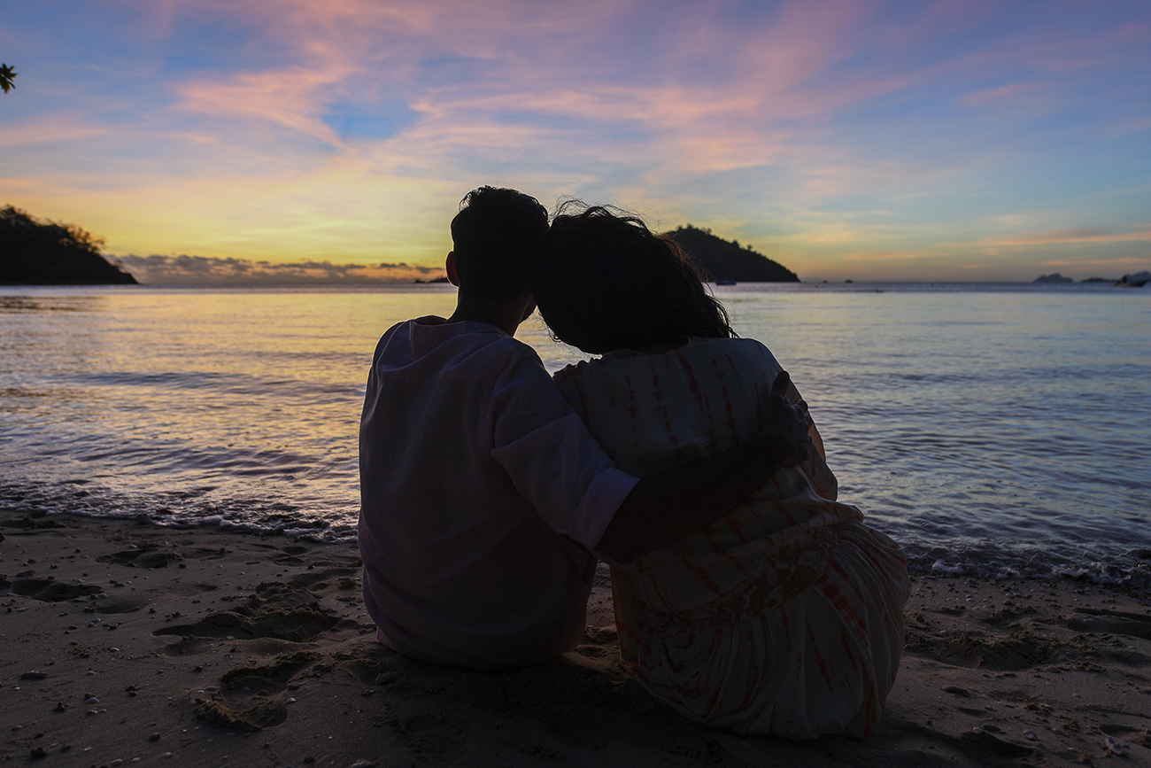 Silhouette of Newly wed couple sit in the sand watching the sunset in Likuliku Fiji