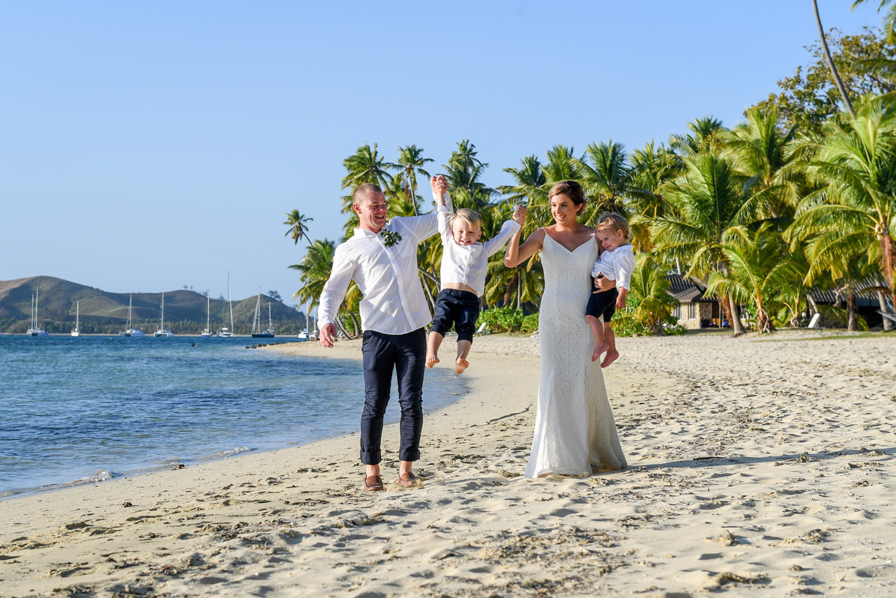 The bride and groom lift their son as they stroll against the palm trees on Fiji Island
