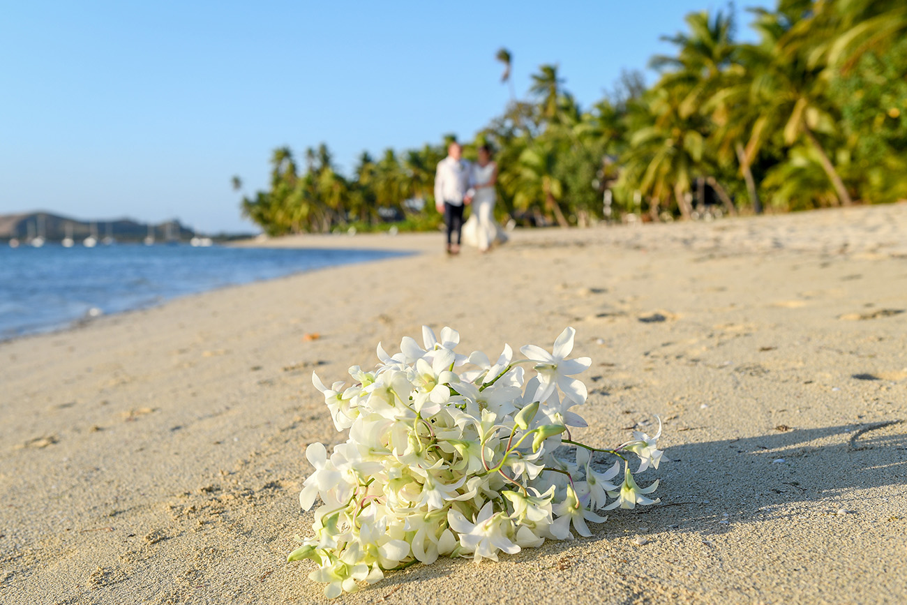 Tropical flower bouquet in the foreground with the married couple in the background
