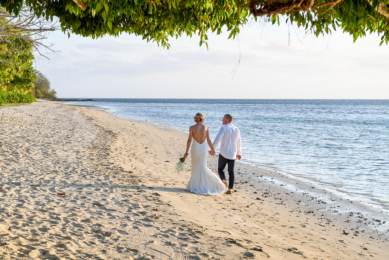 Wideshot of bride and groom strolling hand in hand on the Plantation Island Resort Beach