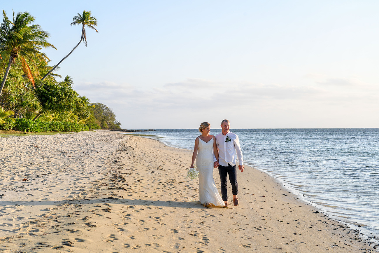 The newly married couple stroll against the palm trees and sea at the Plantation Island Resort Fiji
