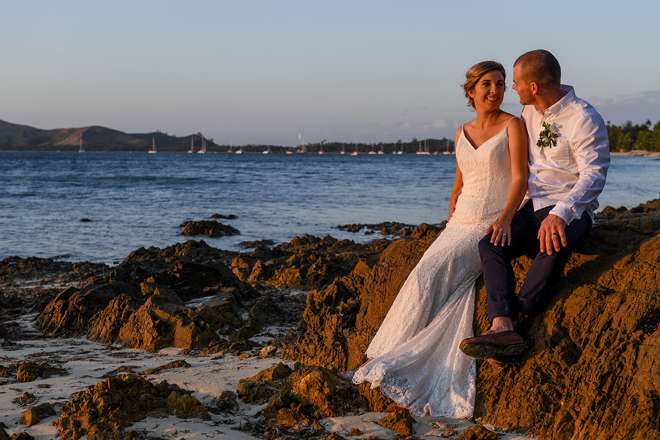 Bride and groom share a moment seated on coral rock