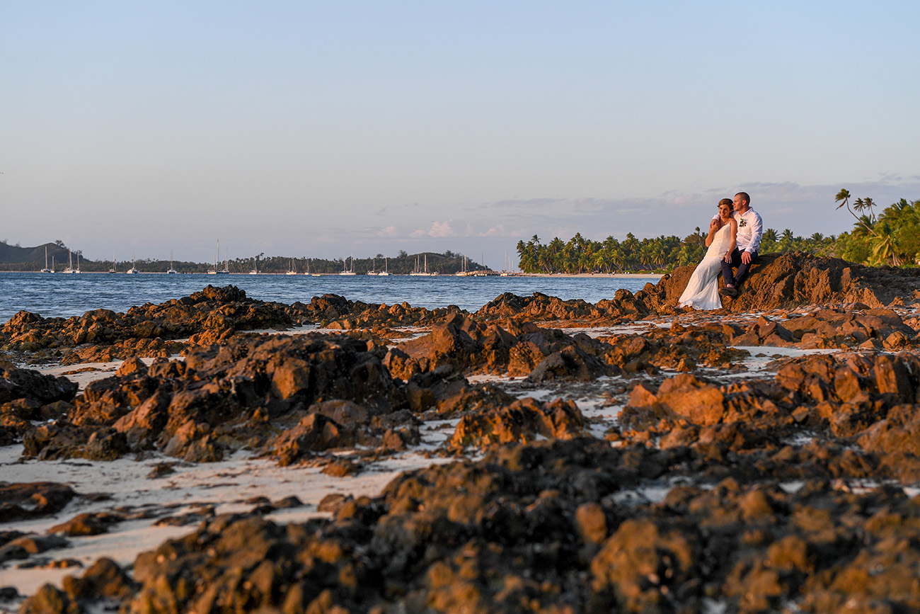 Bride and groom bask on coral rock at Plantation Island Resort Fiji