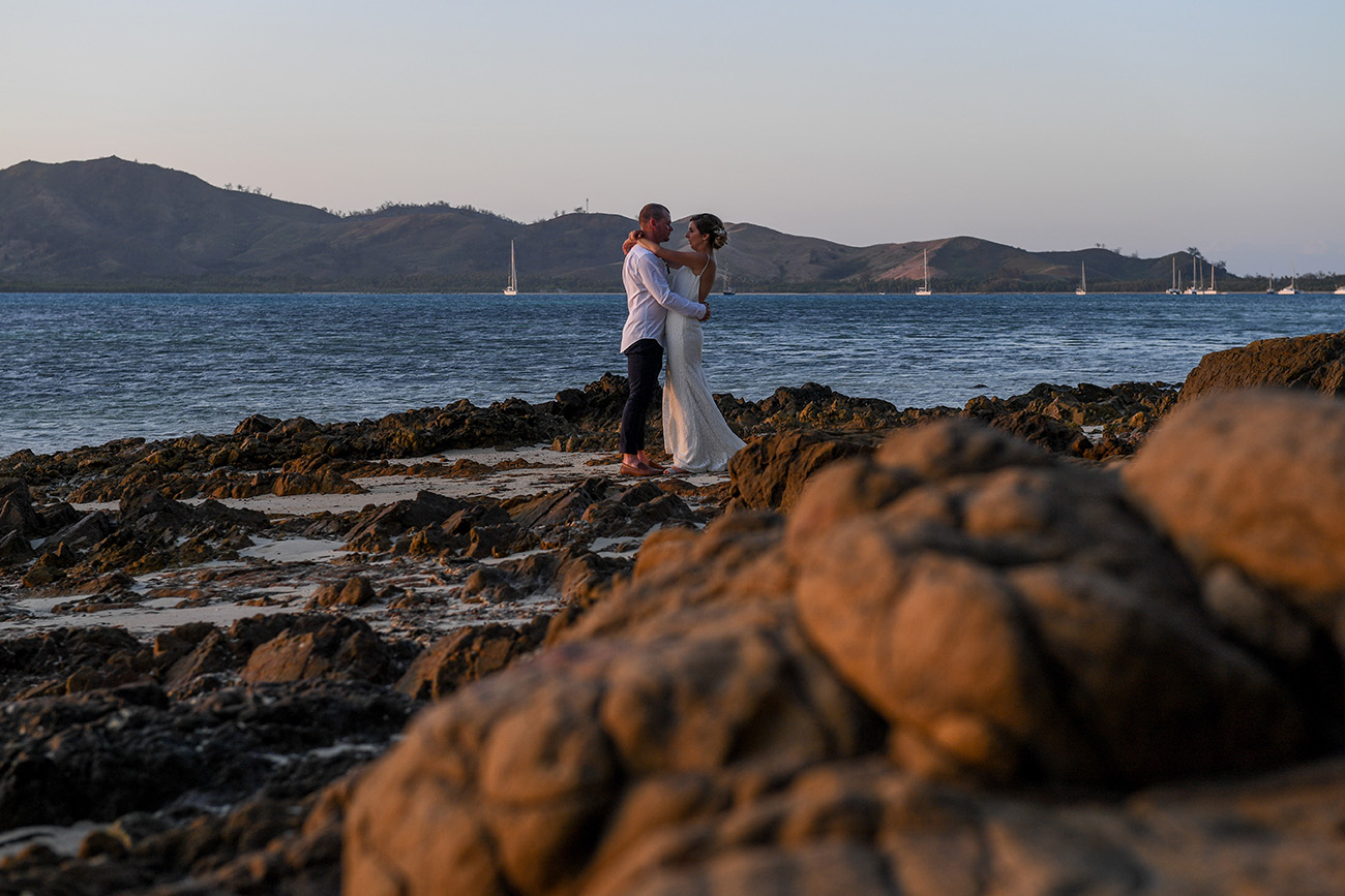 Coral rock in the foreground as Bride and groom dance on coral rocks against the sea