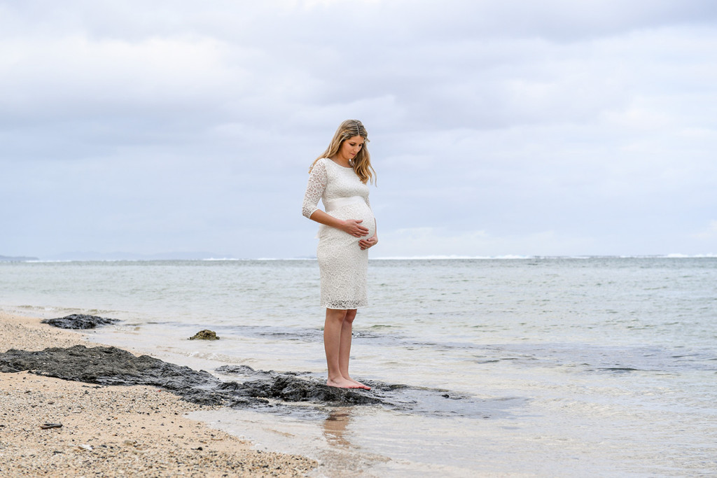 The pregnant bride is looking at her belly standing by the sea on the Fijian beach