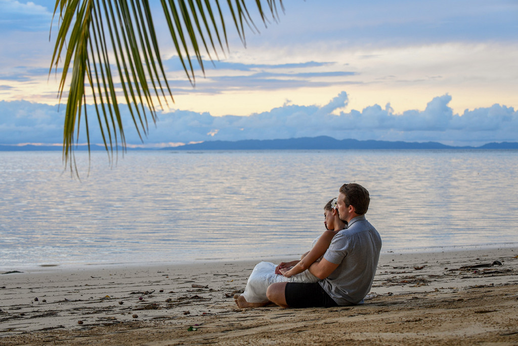 Engaged bride and groom sited on the beach looking at the sea, Matangi Island resort, Fiji