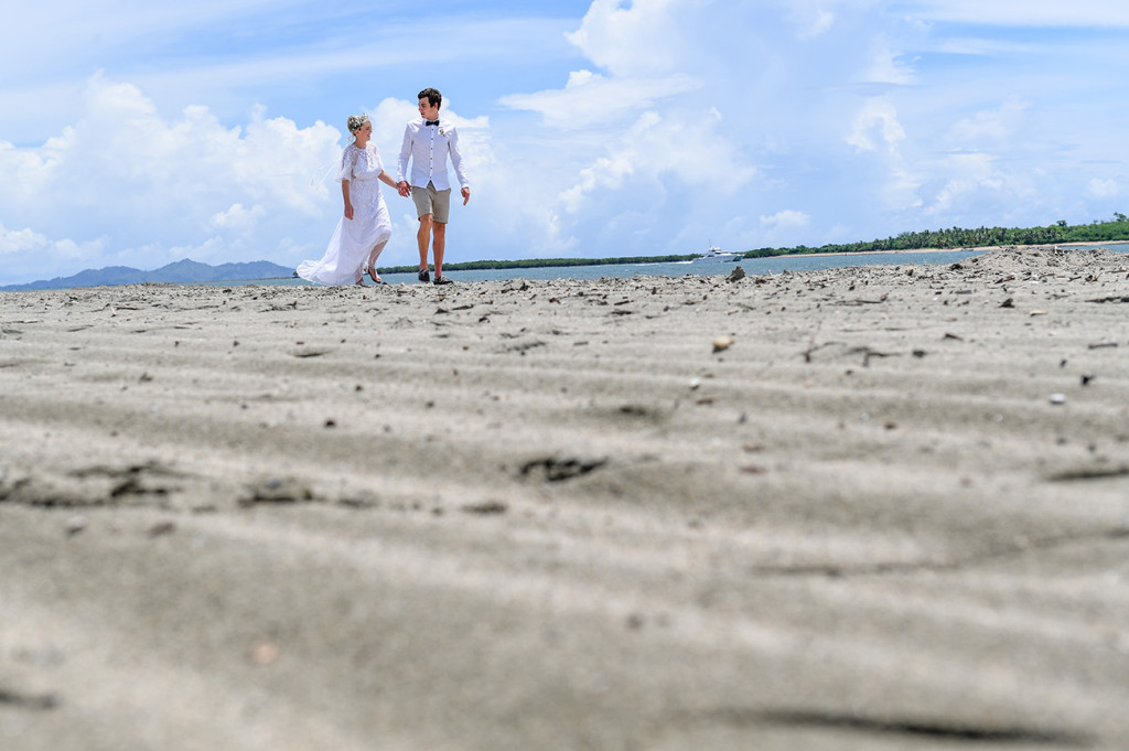 Bride and groom stroll hand in hand on the black sand beach at Denarau Fiji