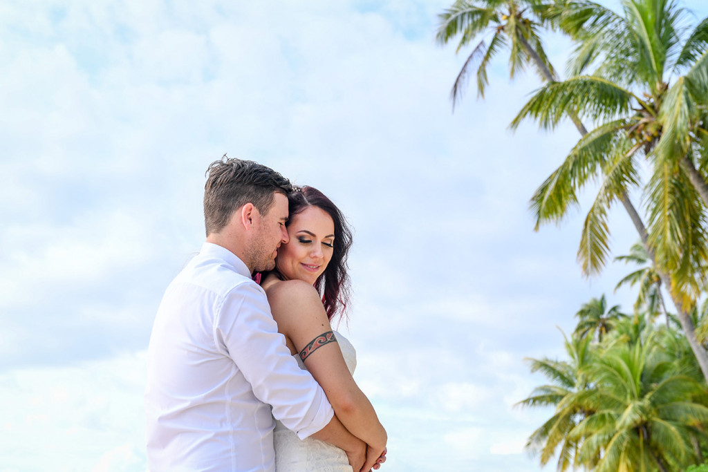 Bride and groom cuddle against breathtaking Fiji palm trees and baby blue sky