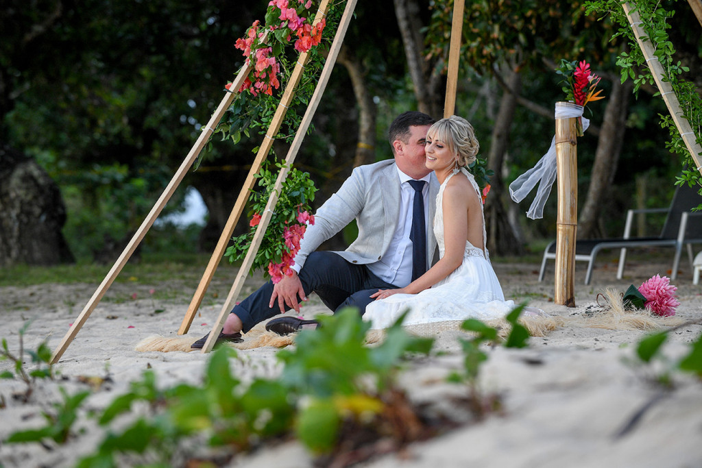 Candid intimate photo of newly weds seated in the sand