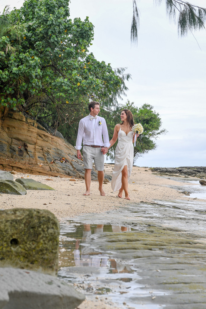 Happily married bride and groom happily stroll hand in hand on Maui bay beach
