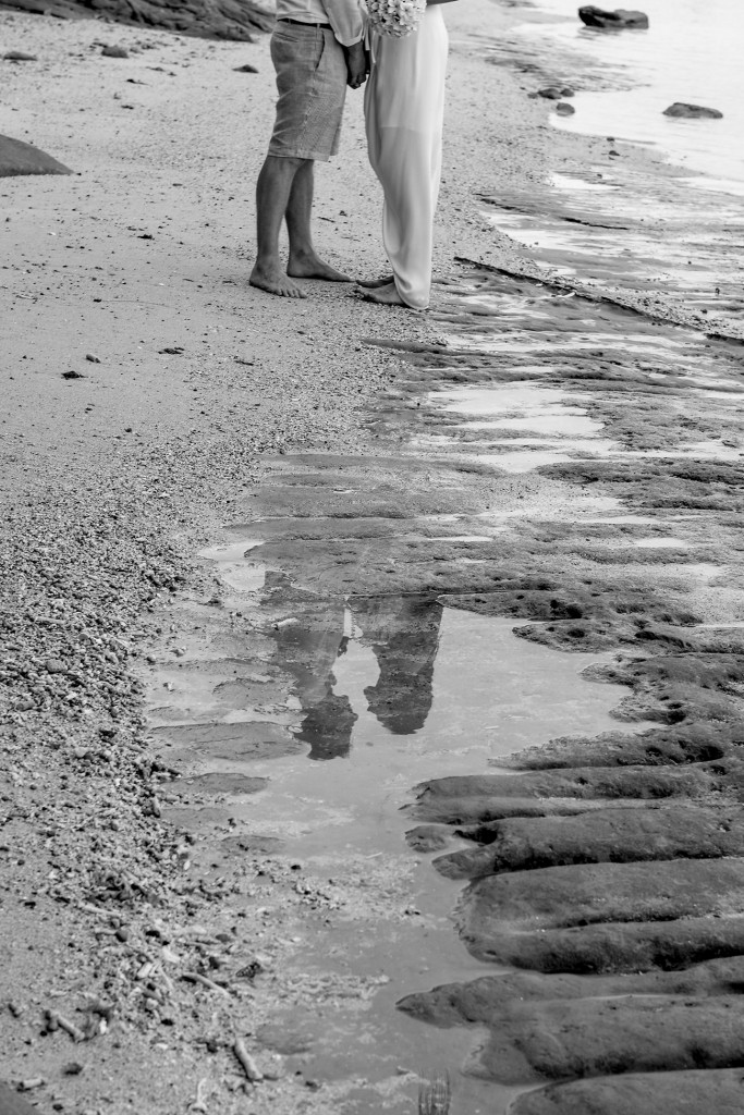 Monochrome reflection of the bride and groom hand in hand on Maui Bay beach