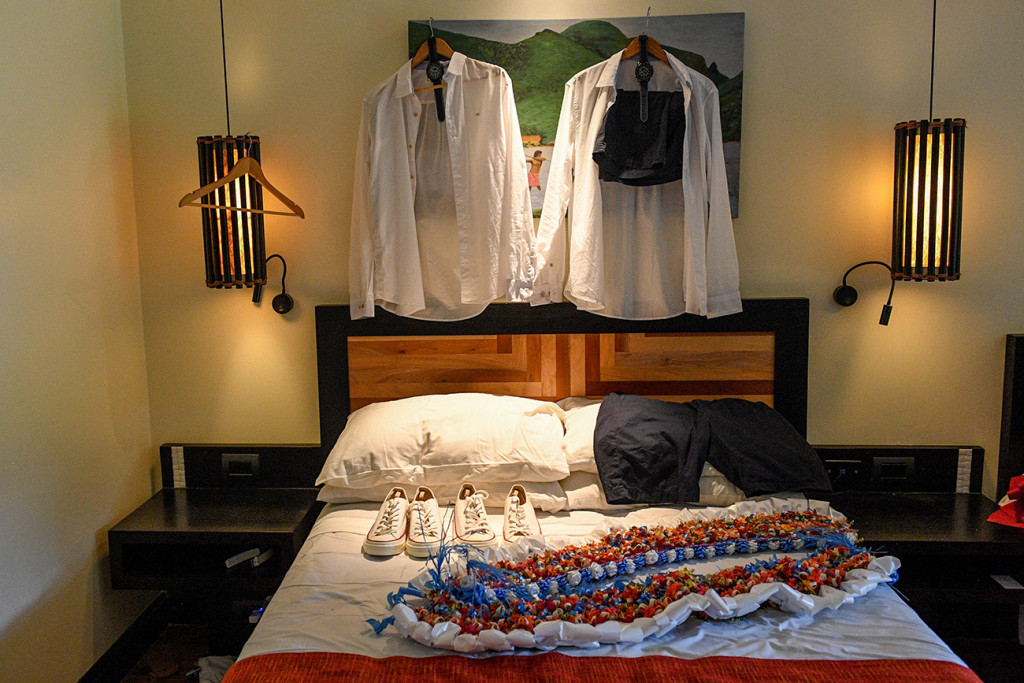 Groomsmen shirts hang in light, sneakers and lei on the bed