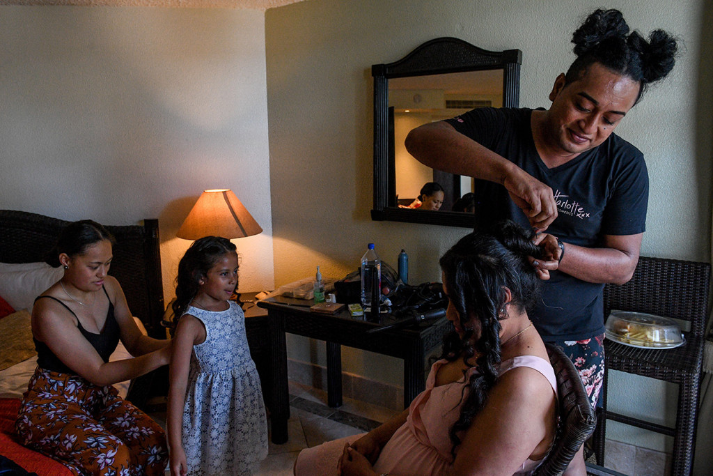A bridesmaid gets her hair done while a flower girl gets her dress zipped