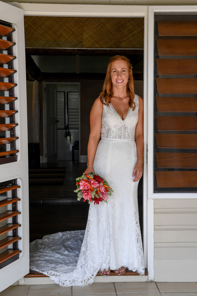 Stunning bride in lace white dress poses at the doorway with her bouquet