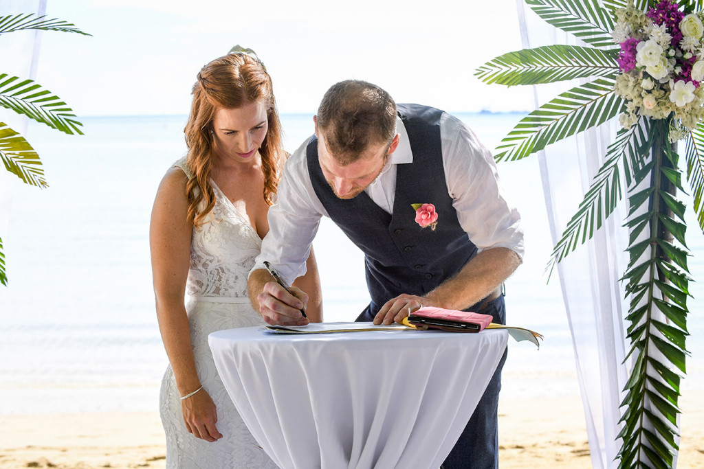 The newly married couple sign the document at the beach at Musket Cove
