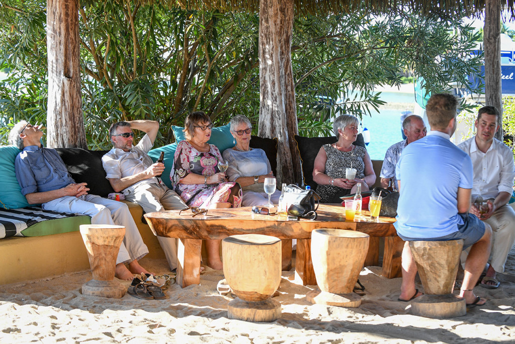 Wedding guests lounge in the sun on palm curved stools by the beach