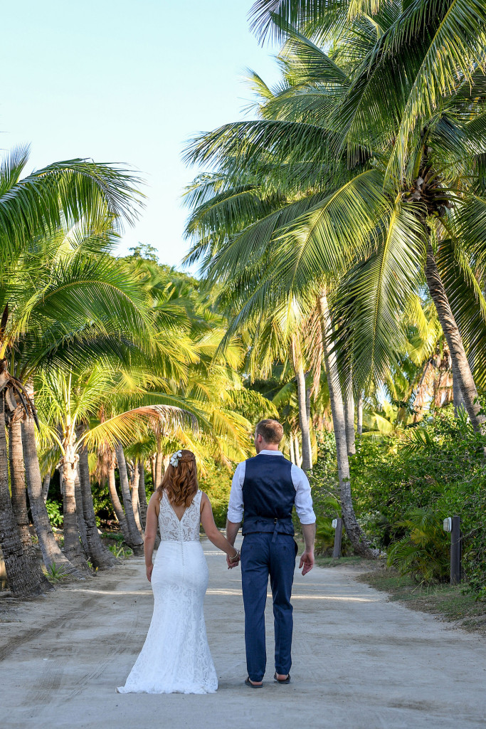 Lofty green Fiji Palm trees sway over the married couple as they stroll around Musket Cover