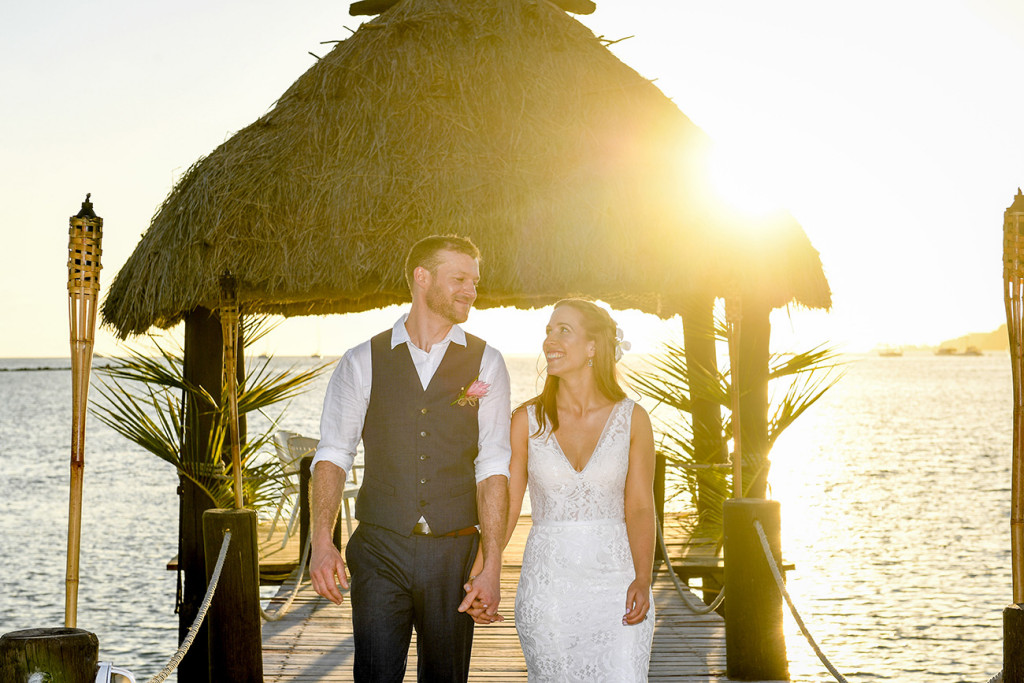 Golden sunlight glows behind the married couple as they walk on the dock